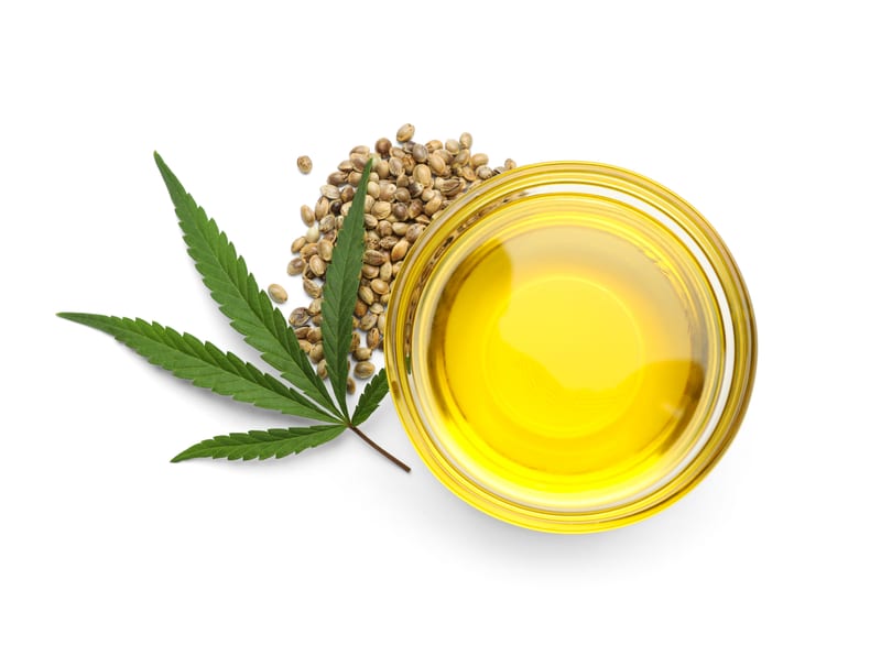 A hemp leaf, hemp seeds and a bowl of golden hemp-seed oil